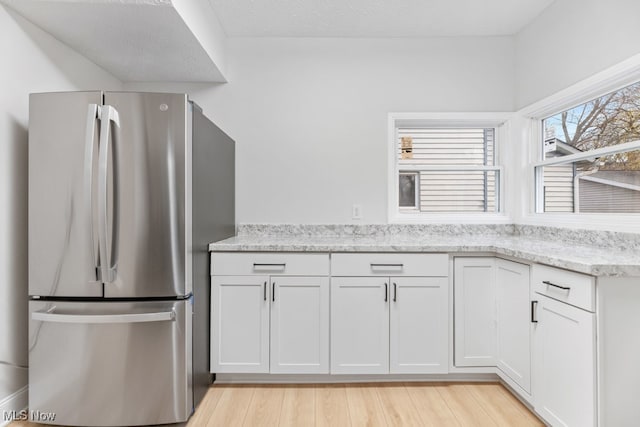 kitchen featuring stainless steel refrigerator, light stone counters, light hardwood / wood-style flooring, and white cabinets