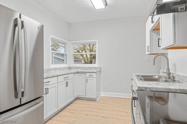 kitchen with light wood-type flooring, a textured ceiling, stainless steel appliances, sink, and white cabinetry