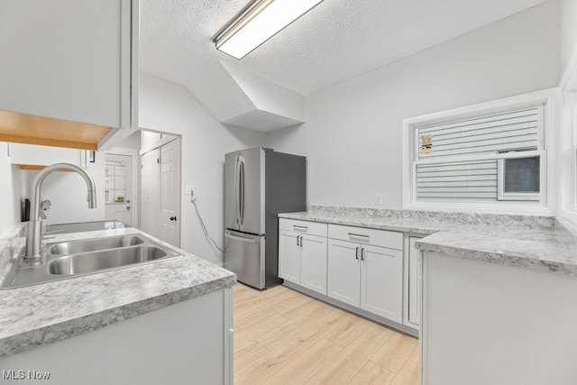 kitchen with stainless steel refrigerator, white cabinetry, sink, light hardwood / wood-style flooring, and a textured ceiling