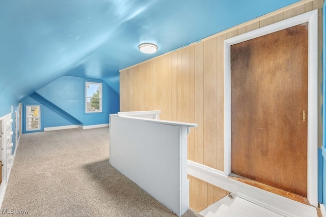 bonus room with wooden walls, light carpet, and vaulted ceiling