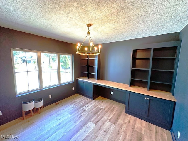 unfurnished office with a chandelier, a textured ceiling, built in desk, and light hardwood / wood-style flooring