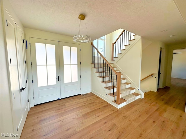 doorway to outside with a textured ceiling, light hardwood / wood-style flooring, and a notable chandelier