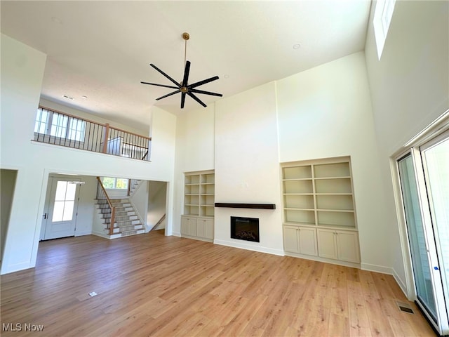 unfurnished living room featuring ceiling fan, light hardwood / wood-style flooring, and a high ceiling