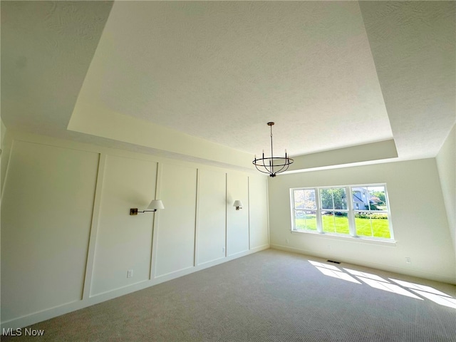 unfurnished bedroom with a tray ceiling, light carpet, a chandelier, and a textured ceiling