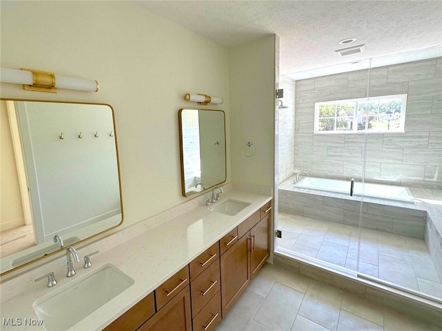 bathroom with tile patterned flooring, a textured ceiling, vanity, and tiled bath