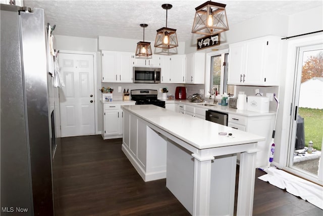 kitchen featuring hanging light fixtures, stainless steel appliances, a kitchen island, dark hardwood / wood-style floors, and white cabinets