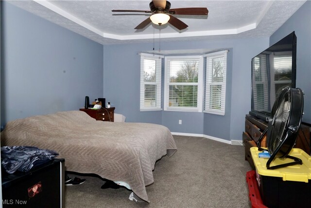 carpeted bedroom with a textured ceiling, a tray ceiling, and ceiling fan