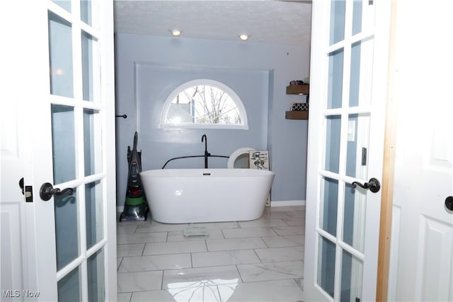 bathroom with a washtub, french doors, and a textured ceiling