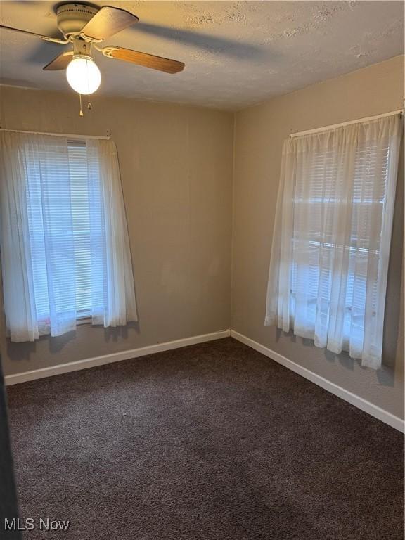 spare room with ceiling fan, a textured ceiling, and dark colored carpet