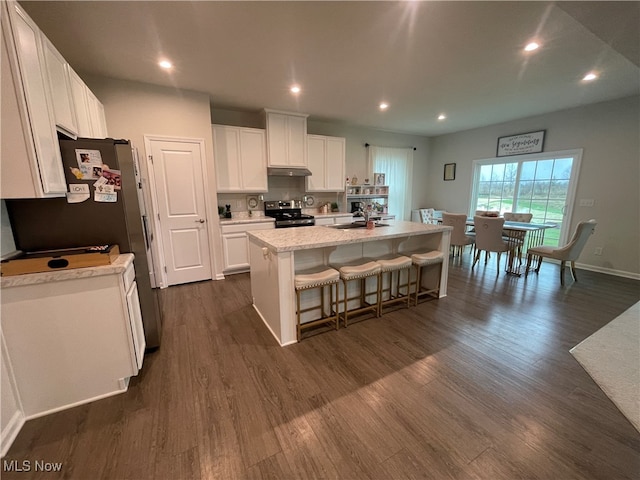 kitchen featuring dark wood-type flooring, a center island with sink, appliances with stainless steel finishes, white cabinetry, and a breakfast bar area