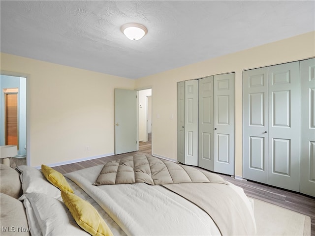 bedroom featuring connected bathroom, multiple closets, light hardwood / wood-style floors, and a textured ceiling