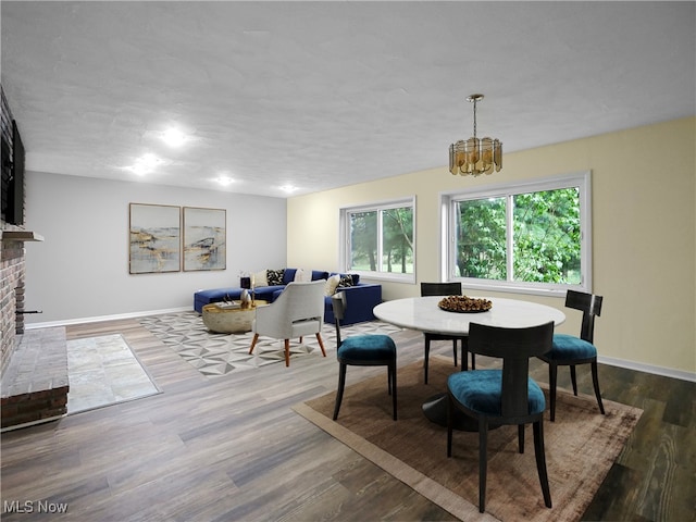 dining area with a chandelier, dark wood-type flooring, and a brick fireplace