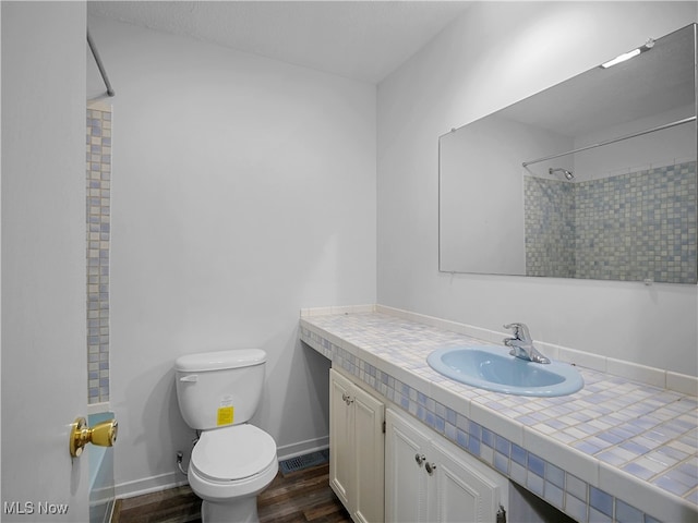 bathroom featuring a tile shower, vanity, hardwood / wood-style flooring, and toilet