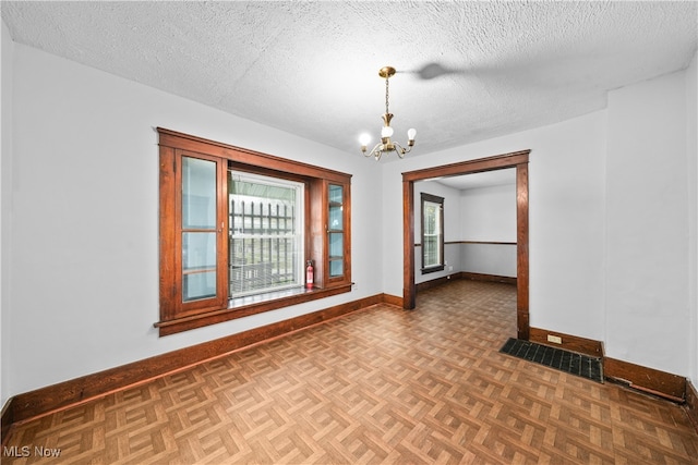 spare room with a chandelier, dark parquet flooring, and a textured ceiling