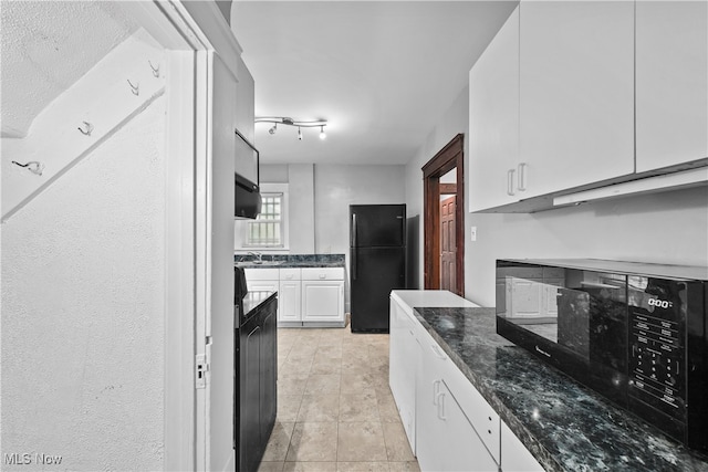 kitchen with dark stone counters, sink, black appliances, light tile patterned floors, and white cabinets