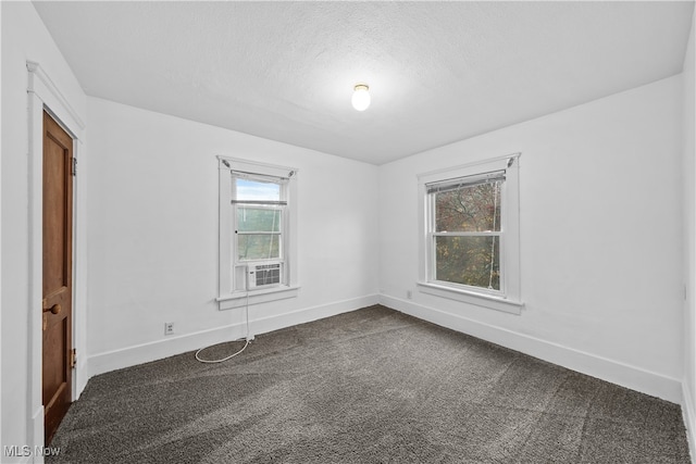 spare room featuring a healthy amount of sunlight, a textured ceiling, and dark carpet