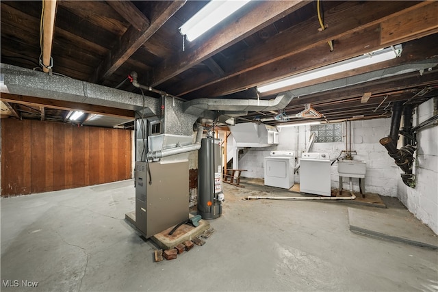 basement featuring washer and clothes dryer, wood walls, gas water heater, sink, and heating unit