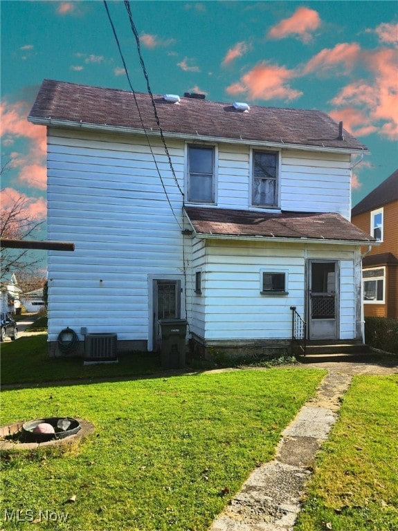 back house at dusk featuring central AC unit and a yard