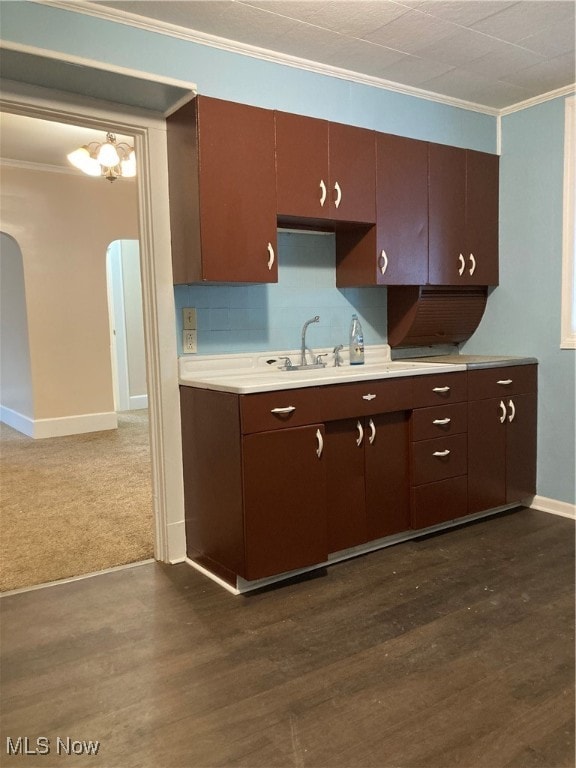 kitchen with dark hardwood / wood-style flooring, backsplash, dark brown cabinets, crown molding, and sink