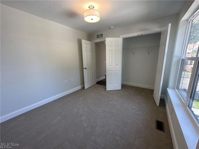 unfurnished bedroom featuring carpet flooring, a closet, a textured ceiling, and multiple windows