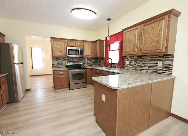 kitchen featuring kitchen peninsula, stainless steel appliances, sink, pendant lighting, and light hardwood / wood-style floors