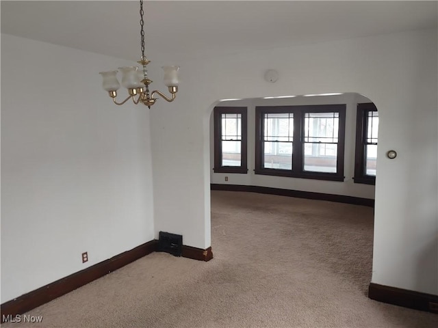 unfurnished dining area featuring arched walkways, carpet floors, a notable chandelier, and baseboards