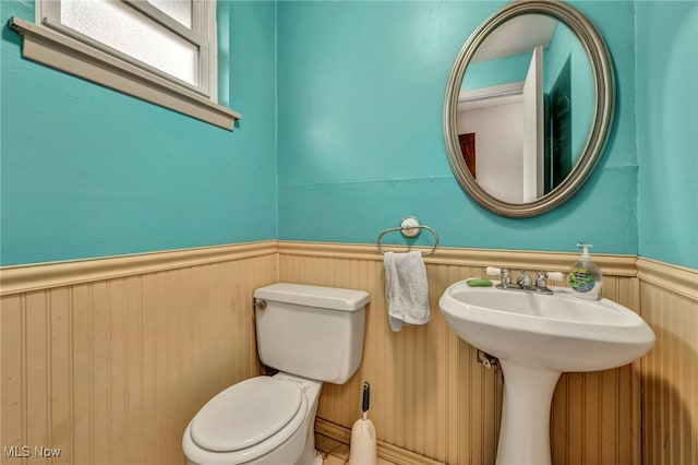 bathroom featuring toilet, sink, and wooden walls