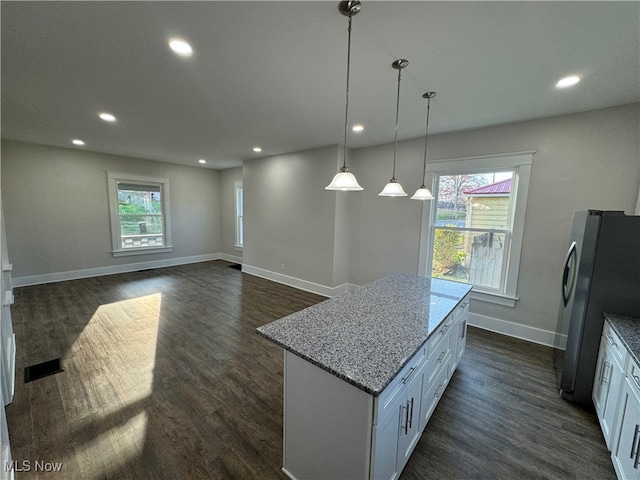 kitchen featuring white cabinetry, stainless steel fridge, hanging light fixtures, and light stone counters