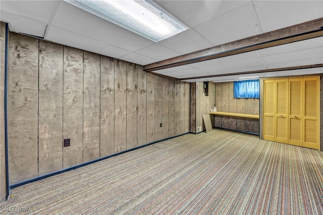 basement with wood walls, a drop ceiling, and light carpet