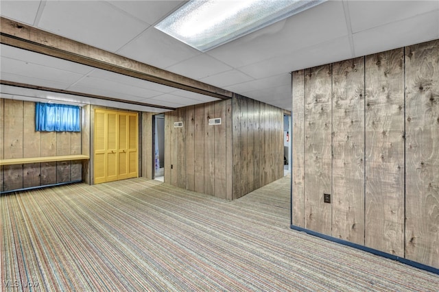 basement featuring light carpet, a paneled ceiling, and wood walls