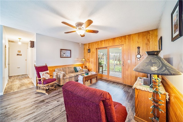 living room with wood walls, ceiling fan, wood-type flooring, and a textured ceiling