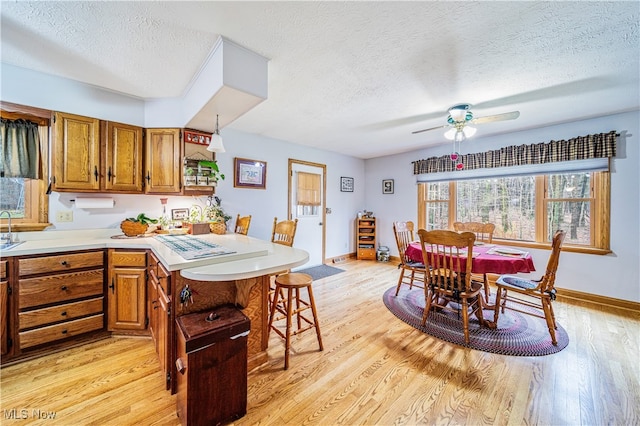 kitchen with a kitchen bar, ceiling fan, light hardwood / wood-style flooring, and a textured ceiling