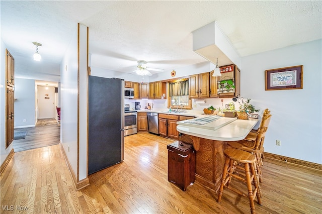 kitchen featuring sink, light hardwood / wood-style flooring, kitchen peninsula, a textured ceiling, and appliances with stainless steel finishes