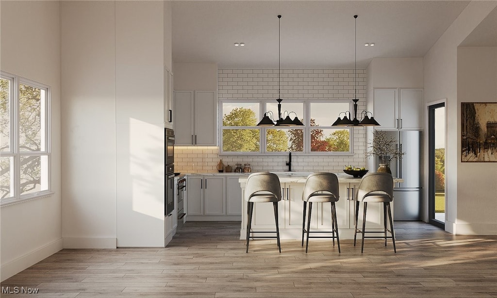 kitchen with pendant lighting, light hardwood / wood-style floors, white cabinets, and a breakfast bar area