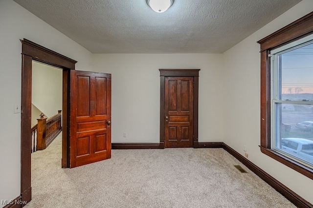 bedroom with light colored carpet, a textured ceiling, and multiple windows