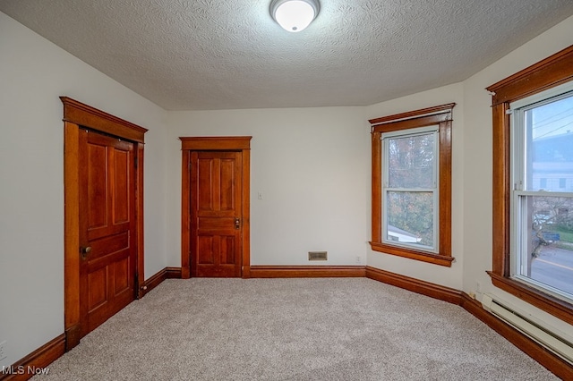 unfurnished bedroom featuring carpet flooring, a textured ceiling, and a baseboard heating unit