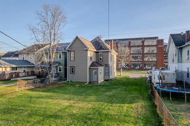 rear view of property with a lawn and a trampoline