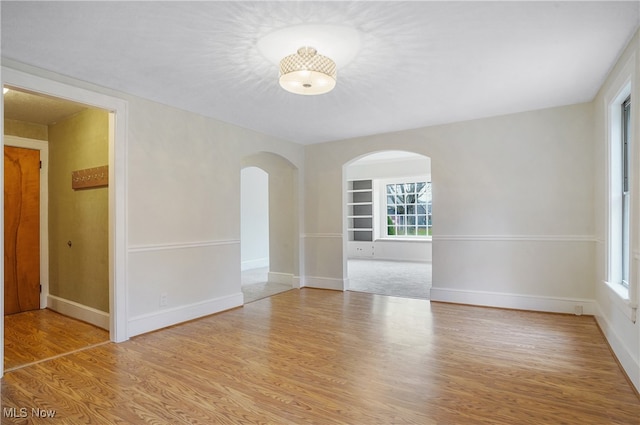 empty room with light wood finished floors, baseboards, and arched walkways