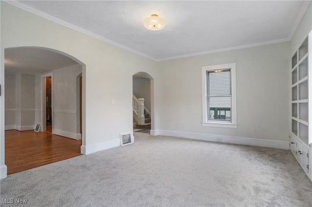 empty room featuring arched walkways, carpet floors, visible vents, baseboards, and ornamental molding