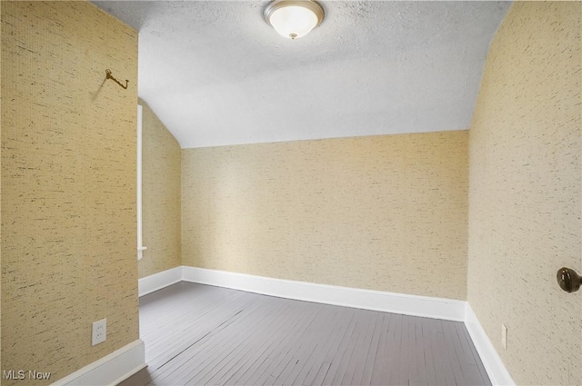 additional living space with lofted ceiling, a textured ceiling, baseboards, and wood finished floors