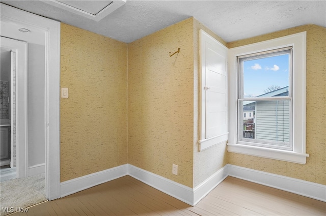 empty room with a textured ceiling, baseboards, and wood finished floors