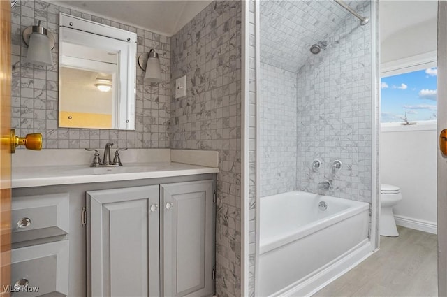 full bath featuring toilet, wood finished floors, vanity, tile walls, and tub / shower combination