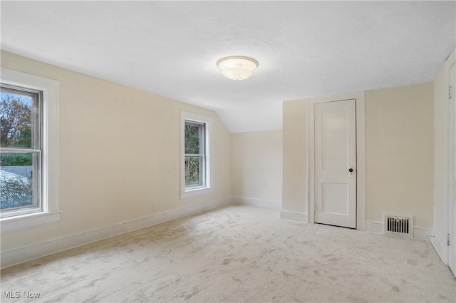 empty room with lofted ceiling, visible vents, light carpet, a textured ceiling, and baseboards