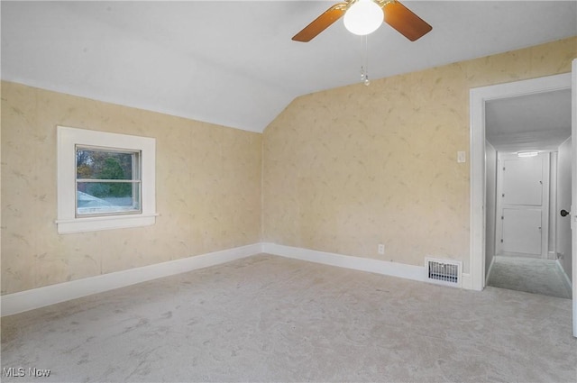 carpeted empty room with lofted ceiling, visible vents, baseboards, and wallpapered walls