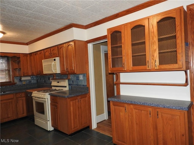 kitchen with brown cabinets, dark countertops, glass insert cabinets, ornamental molding, and white appliances