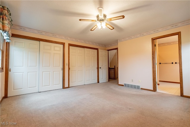 unfurnished bedroom featuring two closets, light colored carpet, ceiling fan, and ornamental molding