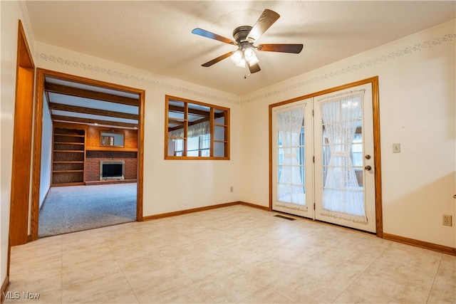 empty room with a fireplace, built in features, a wealth of natural light, and ceiling fan