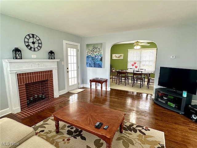 living room featuring ceiling fan, dark hardwood / wood-style floors, and a brick fireplace