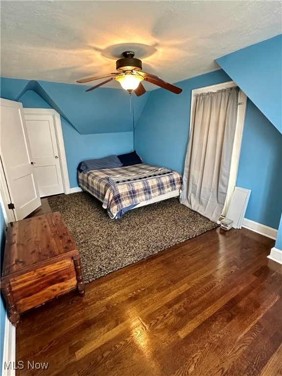 bedroom with vaulted ceiling, ceiling fan, dark wood-type flooring, and a textured ceiling