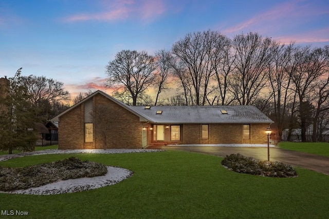 view of front facade with brick siding, curved driveway, and a front yard